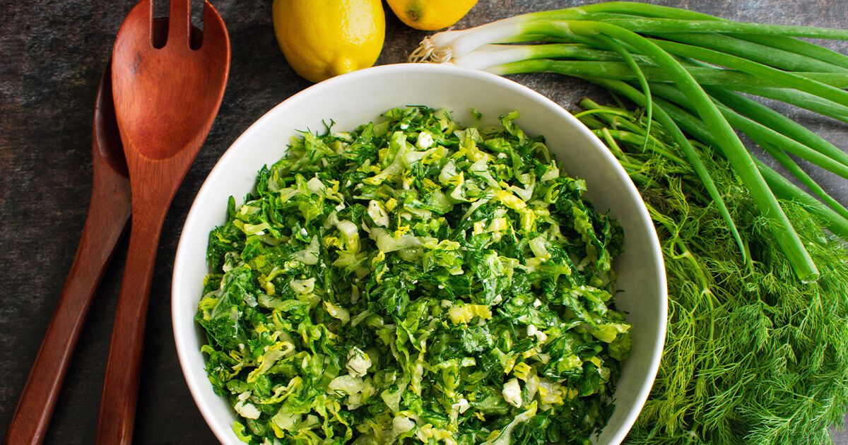 Maroulosalata greek dish with green onion, dill, lemons, and salad serving spoons.